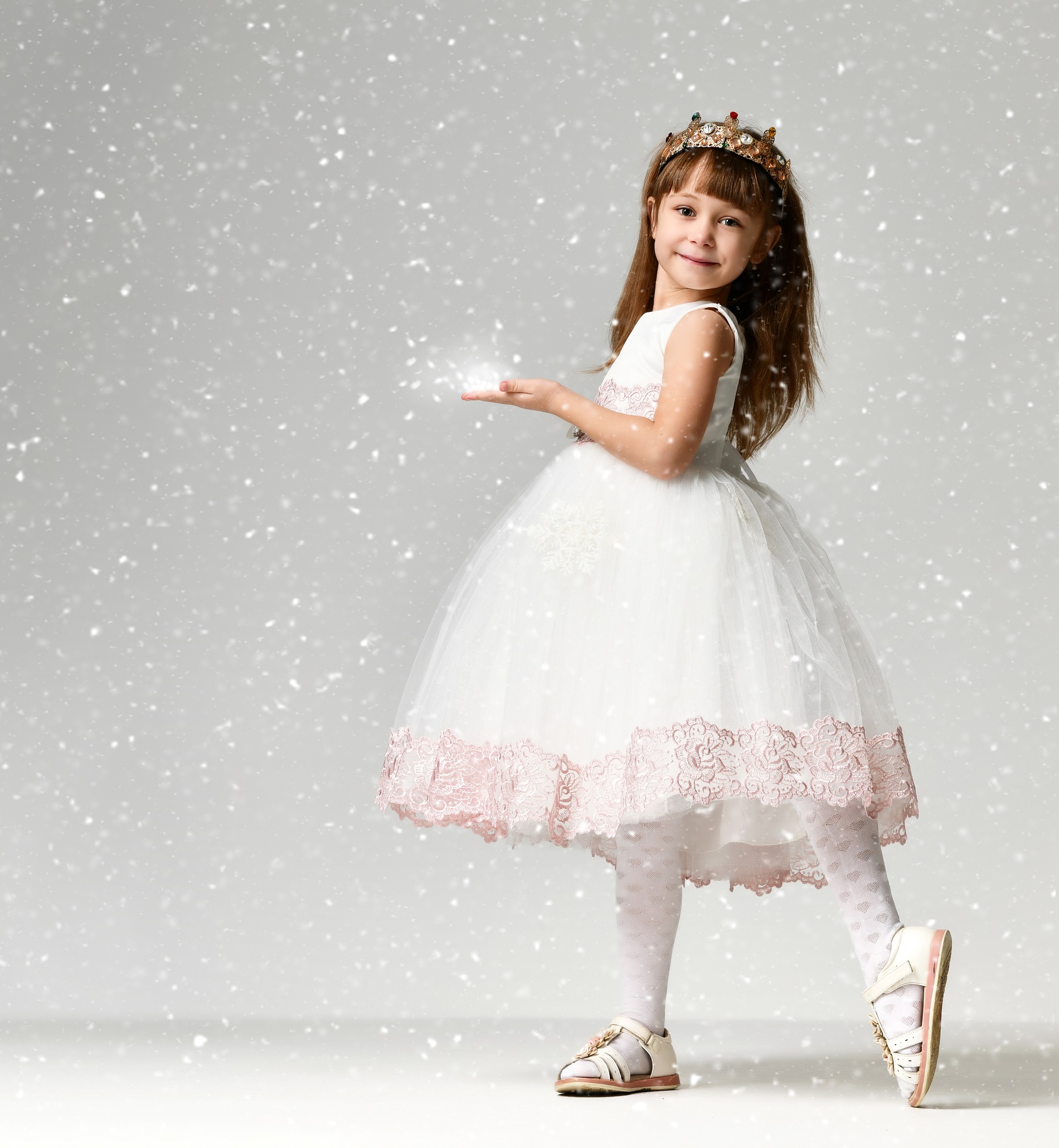 Young little girl model in the white communion winter dress stands in gold crown with expensive gems